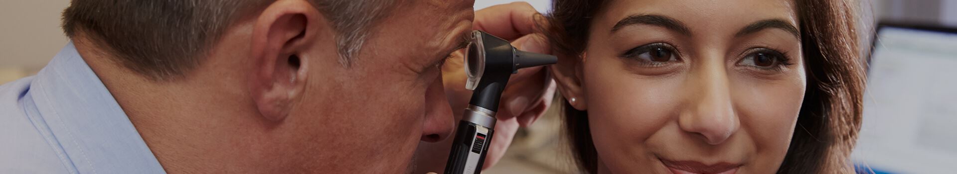 Male physician using an otoscope to look into a female physician's ear