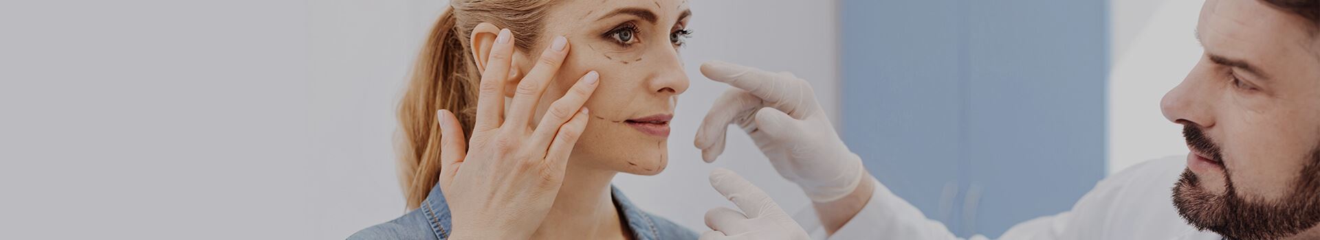 middle aged woman touching her face while consulting with male physician regarding reconstructive surgery